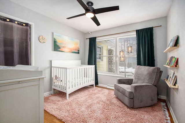 bedroom with baseboard heating, ceiling fan, a nursery area, and light hardwood / wood-style floors