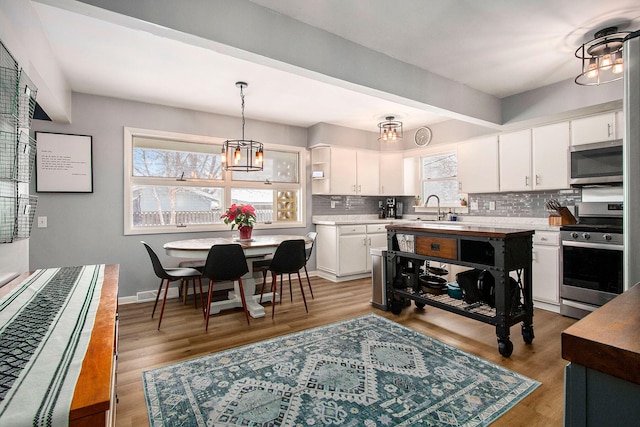 kitchen with backsplash, stainless steel appliances, a chandelier, light hardwood / wood-style floors, and white cabinetry