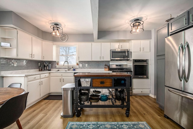 kitchen with pendant lighting, white cabinets, sink, hardwood / wood-style flooring, and appliances with stainless steel finishes