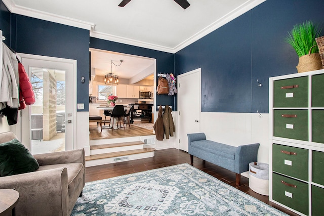 living area with ceiling fan with notable chandelier, dark hardwood / wood-style flooring, and crown molding