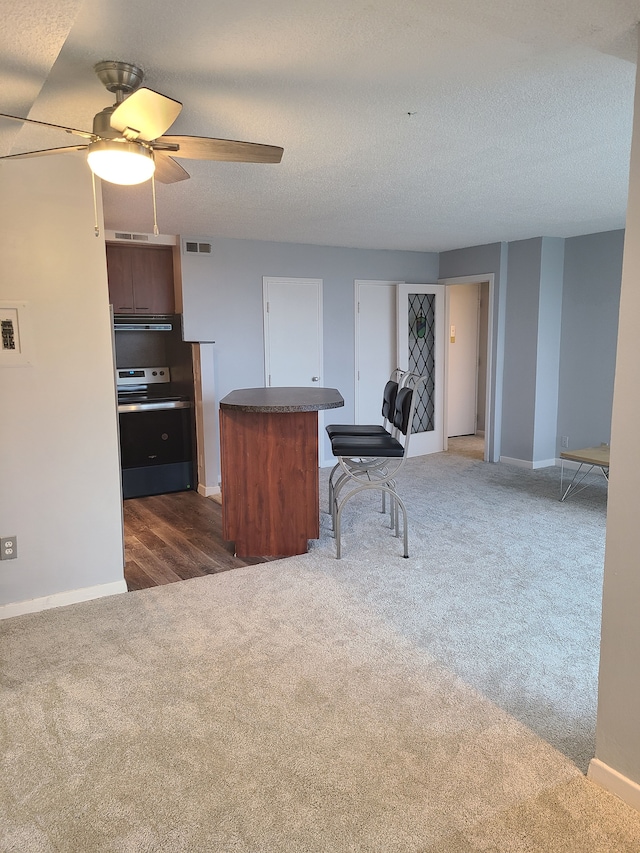 kitchen featuring a textured ceiling, ceiling fan, stainless steel range oven, and dark colored carpet