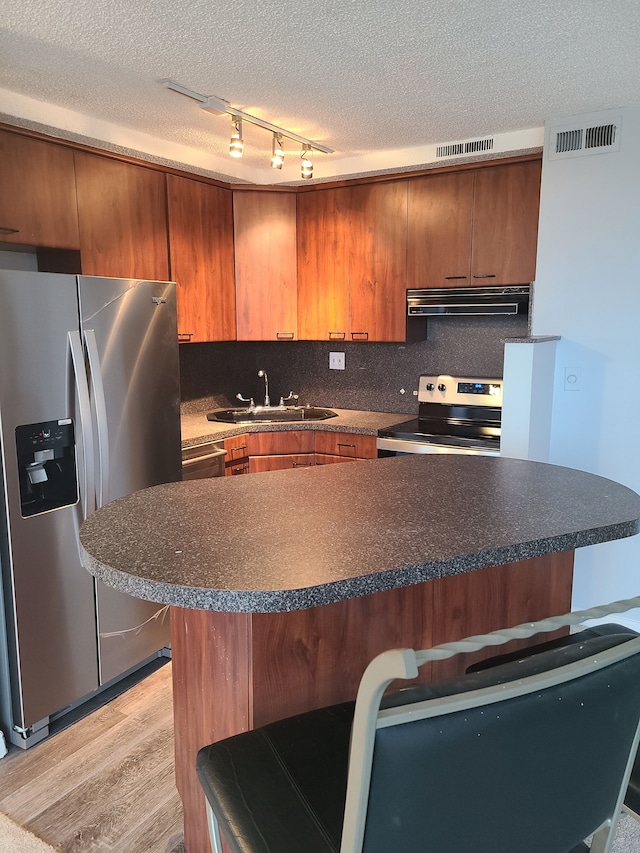 kitchen featuring sink, stainless steel appliances, a textured ceiling, a breakfast bar area, and light wood-type flooring