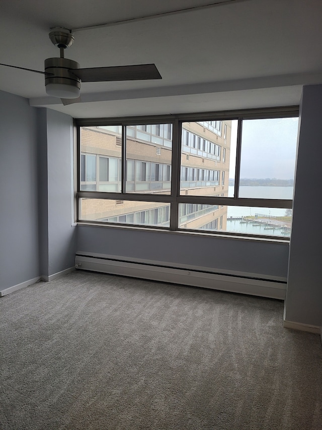 carpeted empty room with a water view, baseboard heating, a healthy amount of sunlight, and ceiling fan