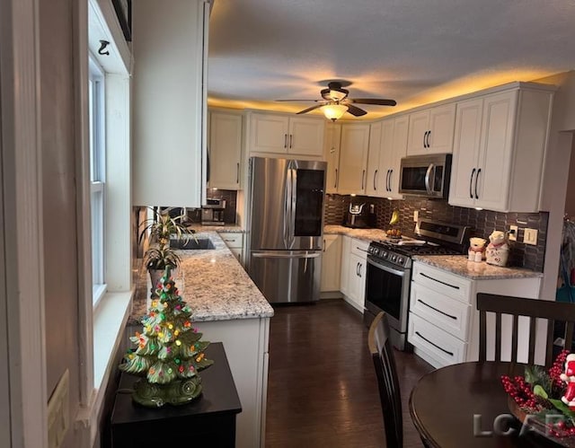 kitchen featuring ceiling fan, dark hardwood / wood-style floors, appliances with stainless steel finishes, light stone counters, and white cabinetry