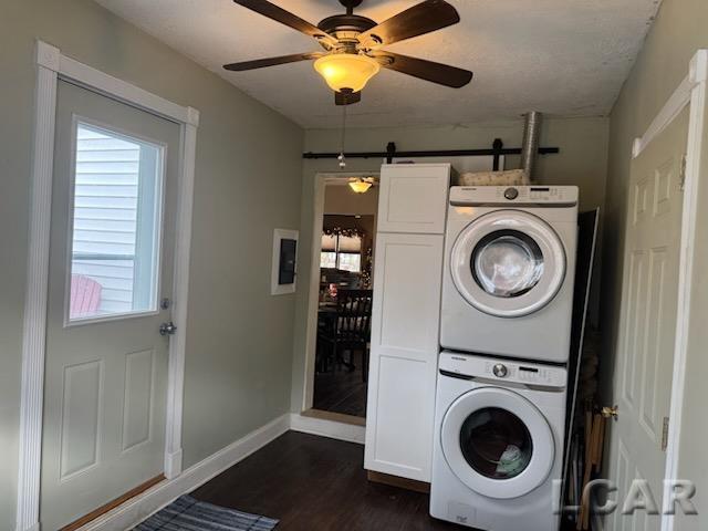 washroom with cabinets, ceiling fan, a barn door, stacked washer / dryer, and dark hardwood / wood-style floors