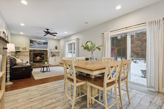 dining room with ceiling fan, a fireplace, and light wood-type flooring