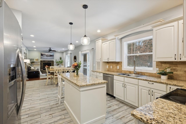 kitchen featuring a stone fireplace, sink, light hardwood / wood-style flooring, appliances with stainless steel finishes, and a kitchen island