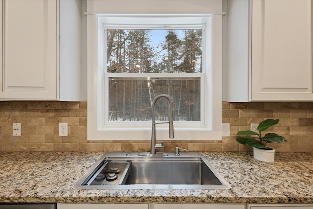 room details with white cabinets, light stone counters, sink, and tasteful backsplash