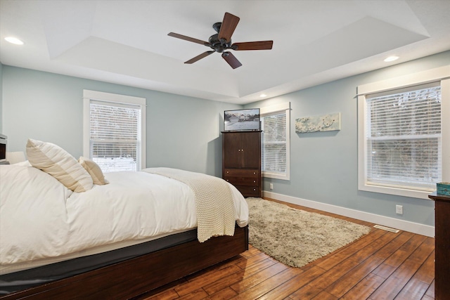 bedroom with hardwood / wood-style floors, ceiling fan, and a tray ceiling