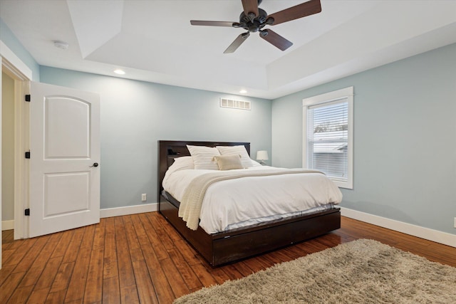 bedroom with dark hardwood / wood-style floors, ceiling fan, and a tray ceiling