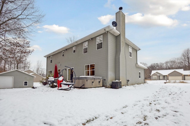 snow covered back of property featuring an outbuilding, a hot tub, a garage, and central air condition unit