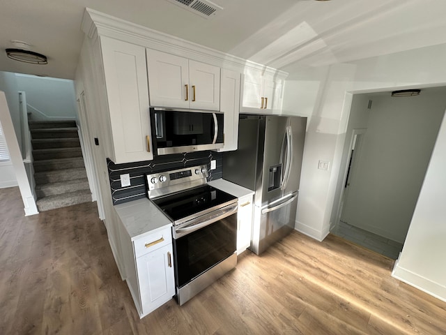 kitchen featuring tasteful backsplash, white cabinetry, light stone counters, light hardwood / wood-style floors, and stainless steel appliances