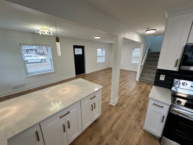 kitchen featuring hanging light fixtures, stainless steel electric range oven, white cabinets, and light hardwood / wood-style flooring