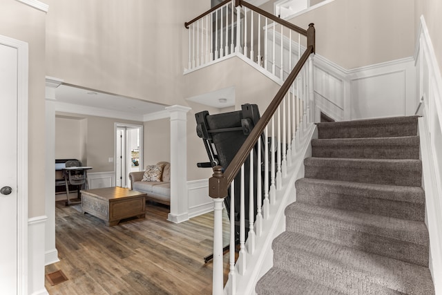 stairway with a towering ceiling, decorative columns, ornamental molding, hardwood / wood-style flooring, and a fireplace