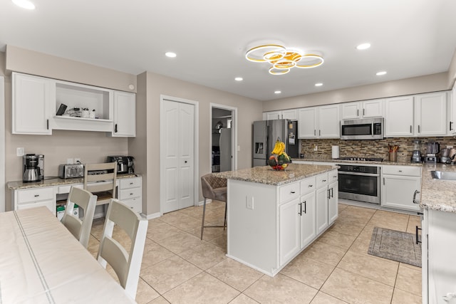 kitchen with white cabinets, appliances with stainless steel finishes, a kitchen island, and light stone counters