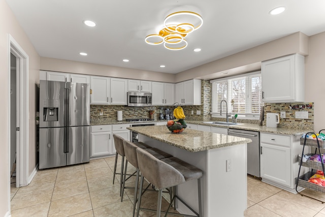 kitchen with appliances with stainless steel finishes, light stone counters, a kitchen island, sink, and white cabinetry