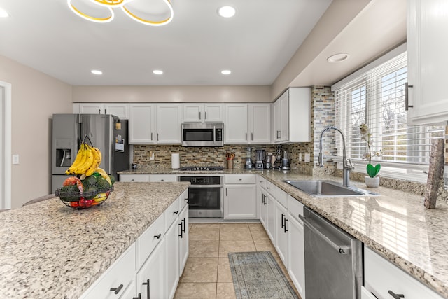 kitchen featuring light stone counters, stainless steel appliances, sink, light tile patterned floors, and white cabinets