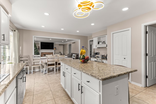 kitchen featuring stainless steel dishwasher, a kitchen island, light stone counters, and white cabinetry