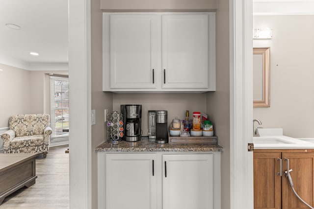 bar featuring light hardwood / wood-style flooring, white cabinetry, and sink