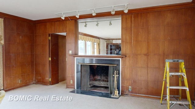 unfurnished living room featuring crown molding, light colored carpet, track lighting, wooden walls, and a fireplace