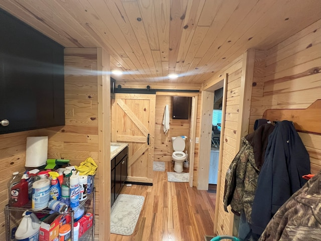 interior space with a barn door, wooden walls, light hardwood / wood-style floors, and wooden ceiling