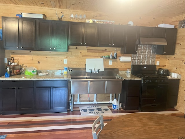 kitchen featuring gas stove, light stone counters, hardwood / wood-style floors, wooden walls, and exhaust hood