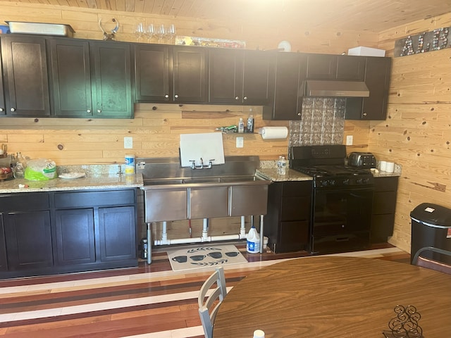 kitchen with wood walls, exhaust hood, black gas stove, light stone countertops, and light wood-type flooring