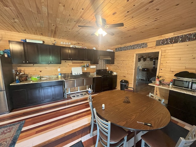 dining space featuring wood walls, ceiling fan, wooden ceiling, and light wood-type flooring