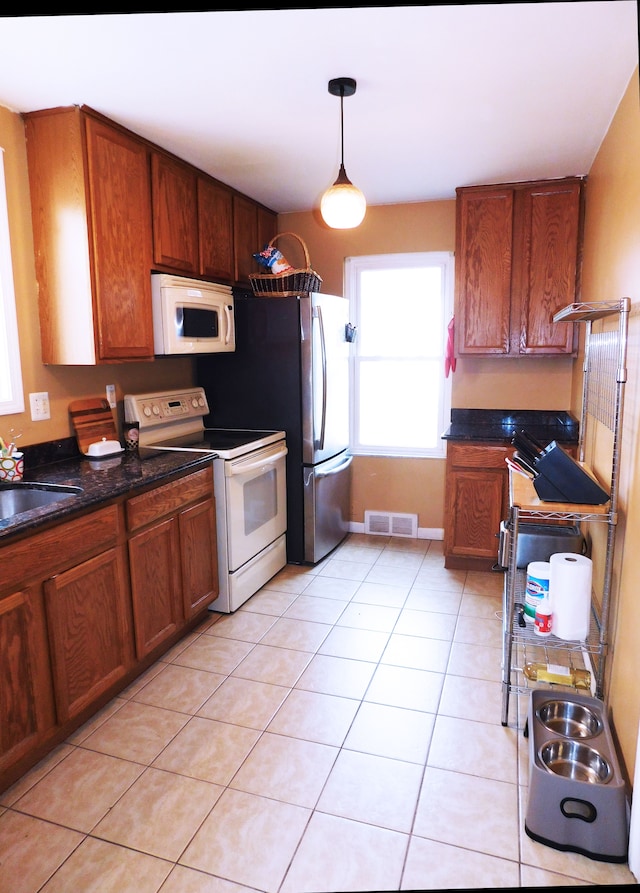 kitchen featuring sink, hanging light fixtures, light tile patterned floors, white appliances, and dark stone counters