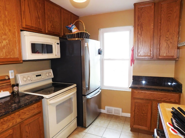 kitchen with light tile patterned flooring, white appliances, and dark stone counters