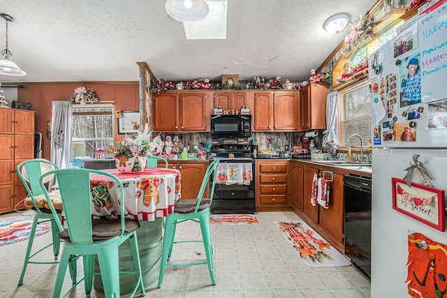 kitchen featuring a skylight, sink, backsplash, pendant lighting, and black appliances