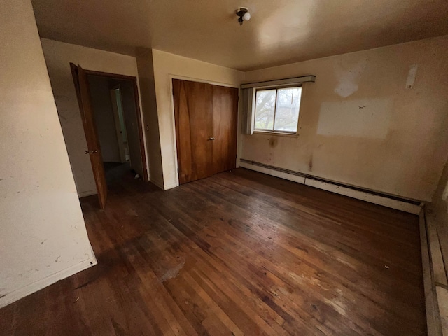 unfurnished bedroom with dark hardwood / wood-style flooring, a closet, and a baseboard heating unit