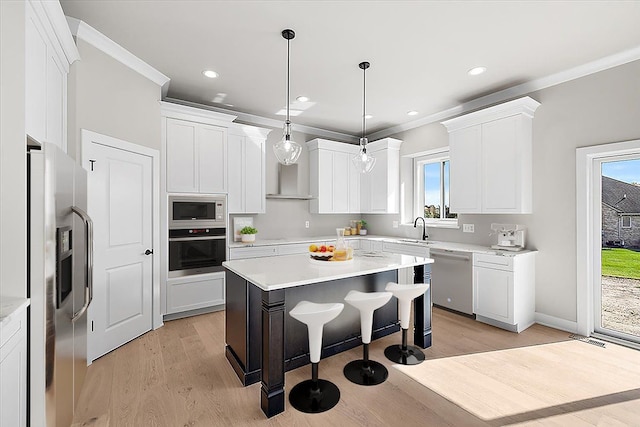 kitchen featuring a kitchen island, white cabinetry, stainless steel appliances, hanging light fixtures, and ornamental molding