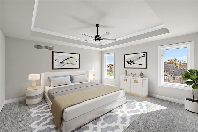 carpeted bedroom featuring ceiling fan, multiple windows, and a tray ceiling