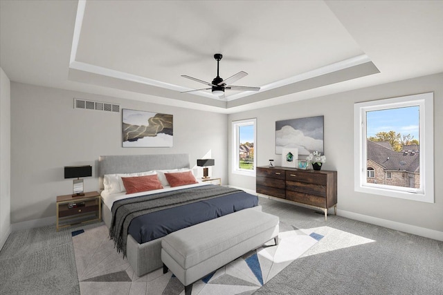 carpeted bedroom with ceiling fan, a tray ceiling, and multiple windows