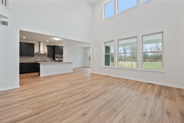 unfurnished living room with a high ceiling, light hardwood / wood-style flooring, and a notable chandelier