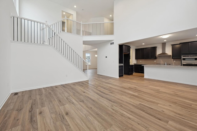 unfurnished living room featuring light wood-type flooring, sink, and a high ceiling