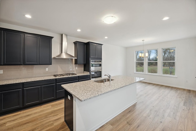 kitchen with sink, wall chimney exhaust hood, light wood-type flooring, and appliances with stainless steel finishes