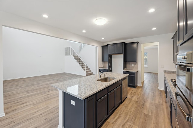 kitchen with sink, light stone counters, stainless steel dishwasher, an island with sink, and light hardwood / wood-style floors