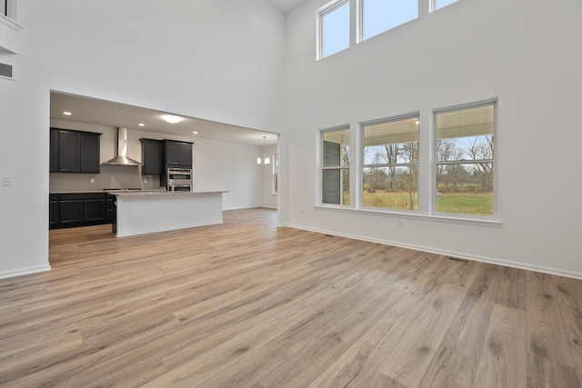 unfurnished living room featuring a towering ceiling, light hardwood / wood-style floors, and an inviting chandelier