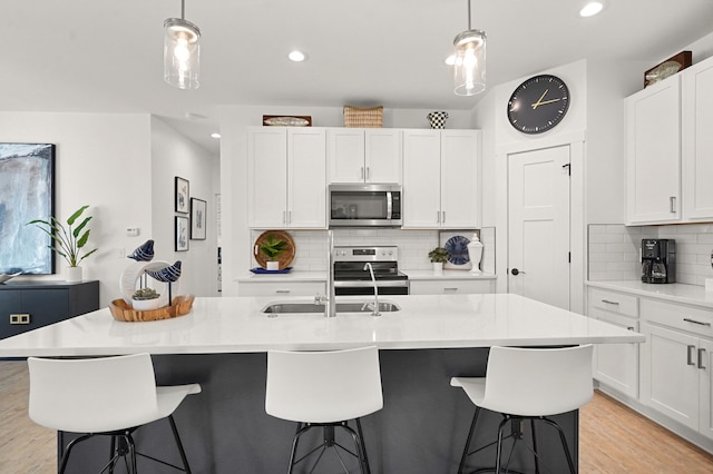 kitchen with decorative backsplash, an island with sink, decorative light fixtures, and appliances with stainless steel finishes