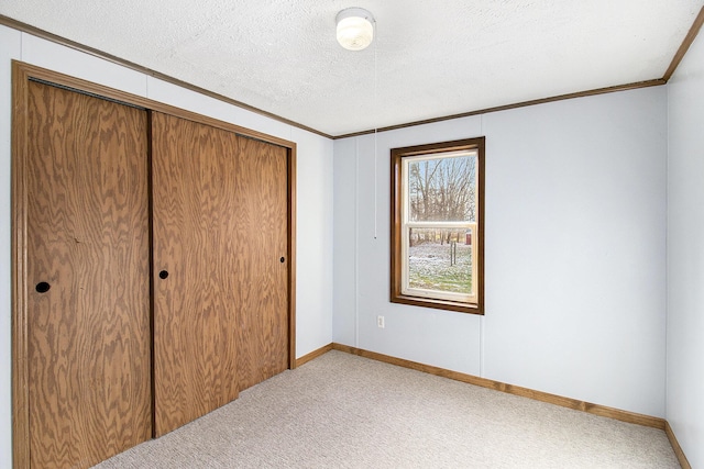 unfurnished bedroom with a textured ceiling, ornamental molding, light carpet, and a closet