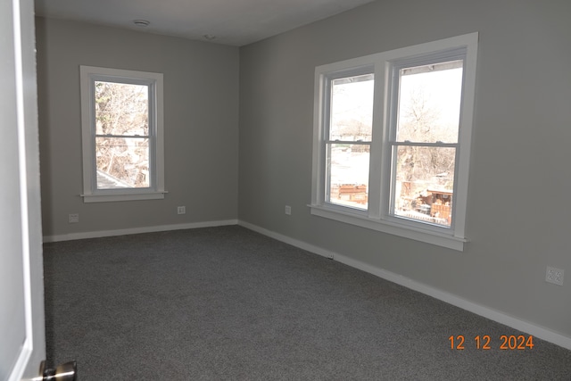 spare room with a wealth of natural light and dark colored carpet