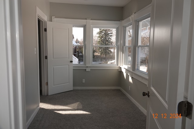 unfurnished room with a healthy amount of sunlight and dark carpet