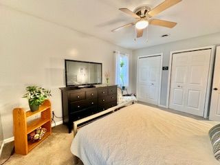 bedroom with ceiling fan, light colored carpet, and multiple closets