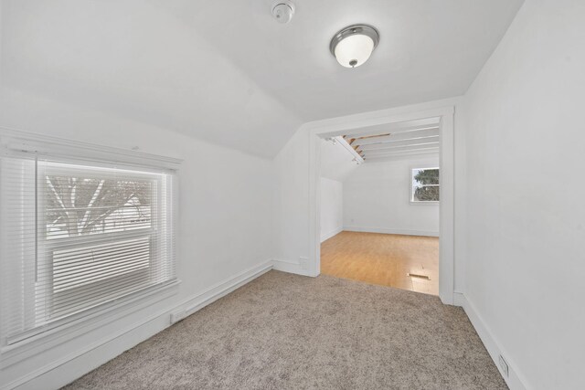 additional living space featuring vaulted ceiling and light carpet