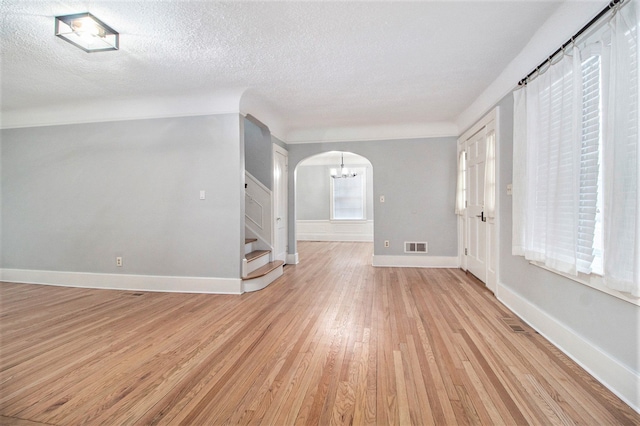 empty room with a textured ceiling, light wood-type flooring, and a healthy amount of sunlight