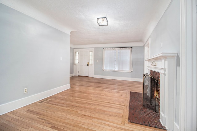 unfurnished living room with a brick fireplace, a textured ceiling, and light hardwood / wood-style flooring