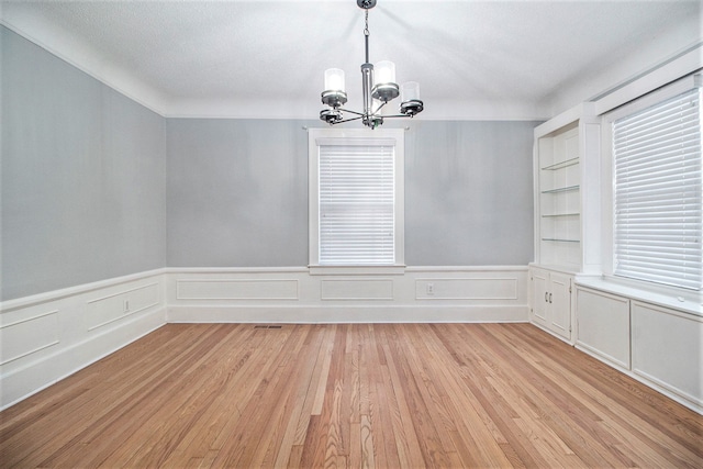 empty room featuring light hardwood / wood-style floors, a healthy amount of sunlight, a textured ceiling, and a chandelier