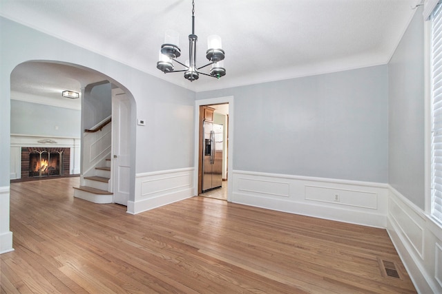 unfurnished dining area with a fireplace, light hardwood / wood-style floors, and an inviting chandelier